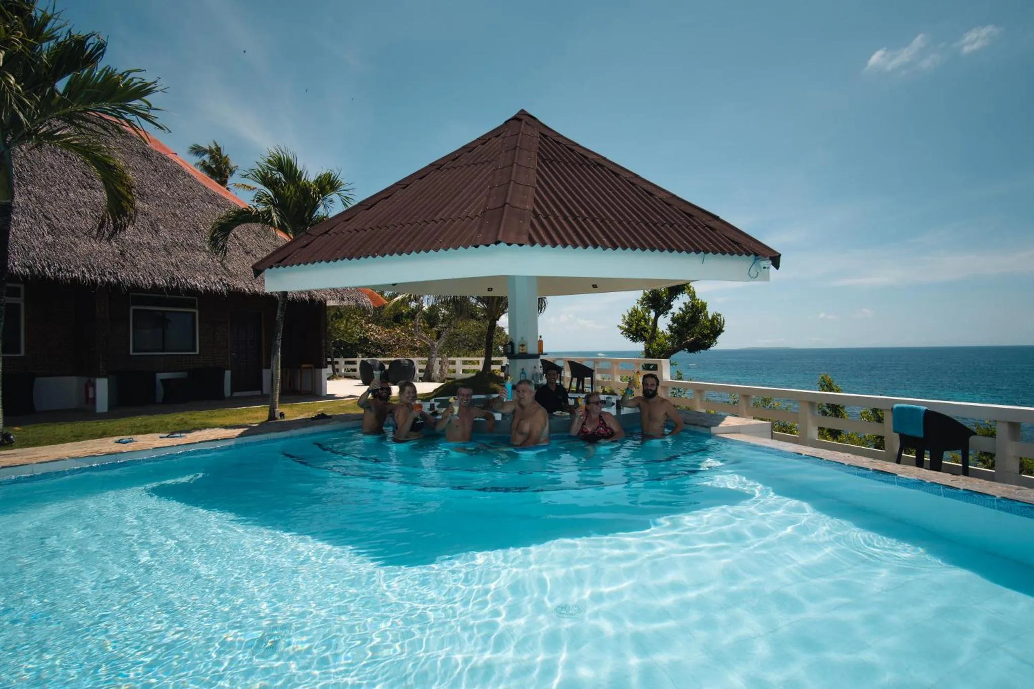 Des personnes se rafraîchissent dans une piscine bordée d'une terrasse ombragée.