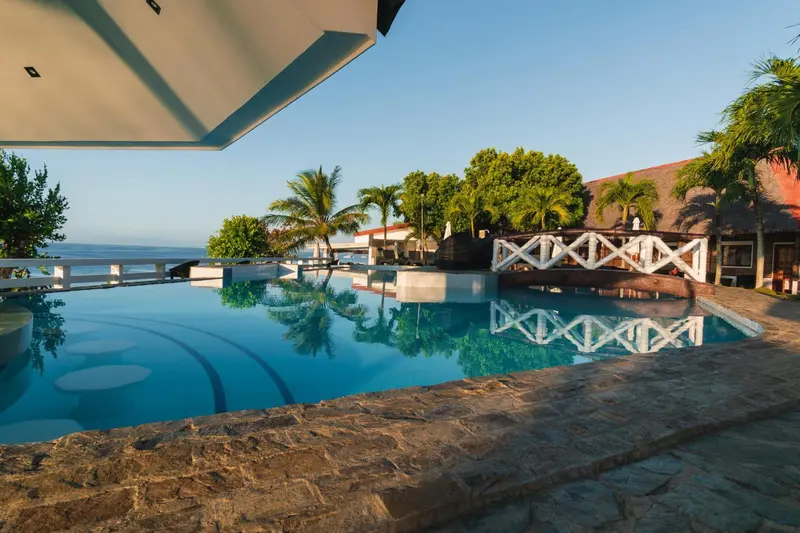 Une piscine bleue reflète le ciel et la végétation tropicale.