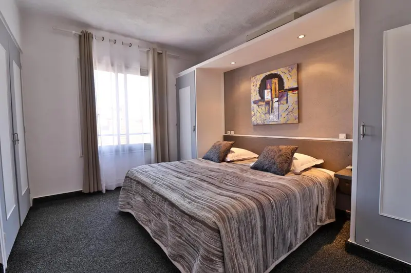 Une chambre avec un grand lit recouvert d'une couverture grise et de coussins.