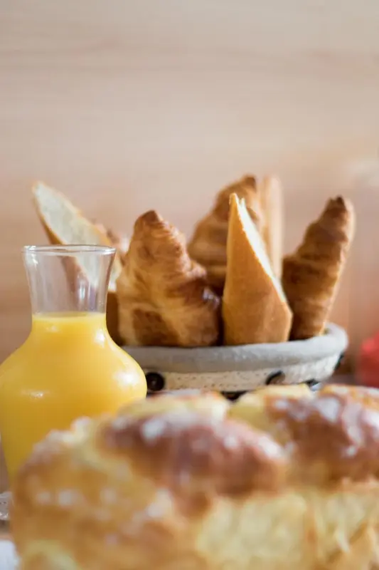 Une corbeille de viennoiseries et un pichet de jus d'orange sont présentés sur une table.