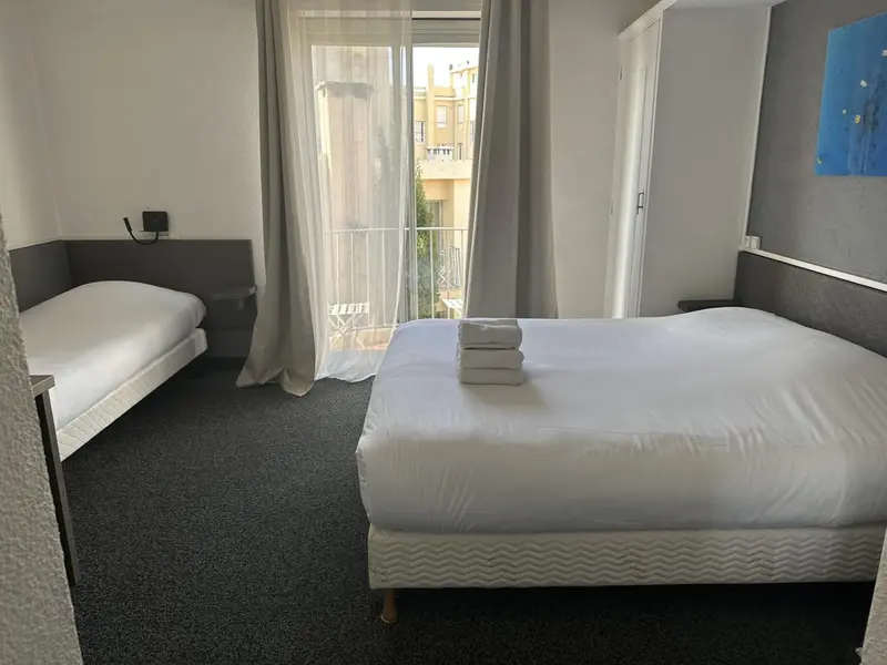 Une chambre lumineuse avec deux lits et une porte-fenêtre donnant sur un balcon.