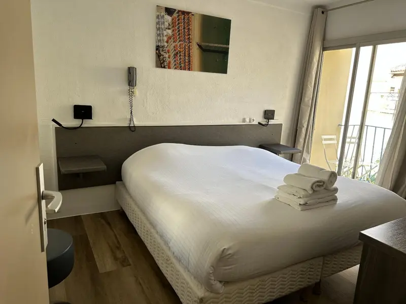 Une chambre lumineuse avec un lit blanc et un accès à un balcon.