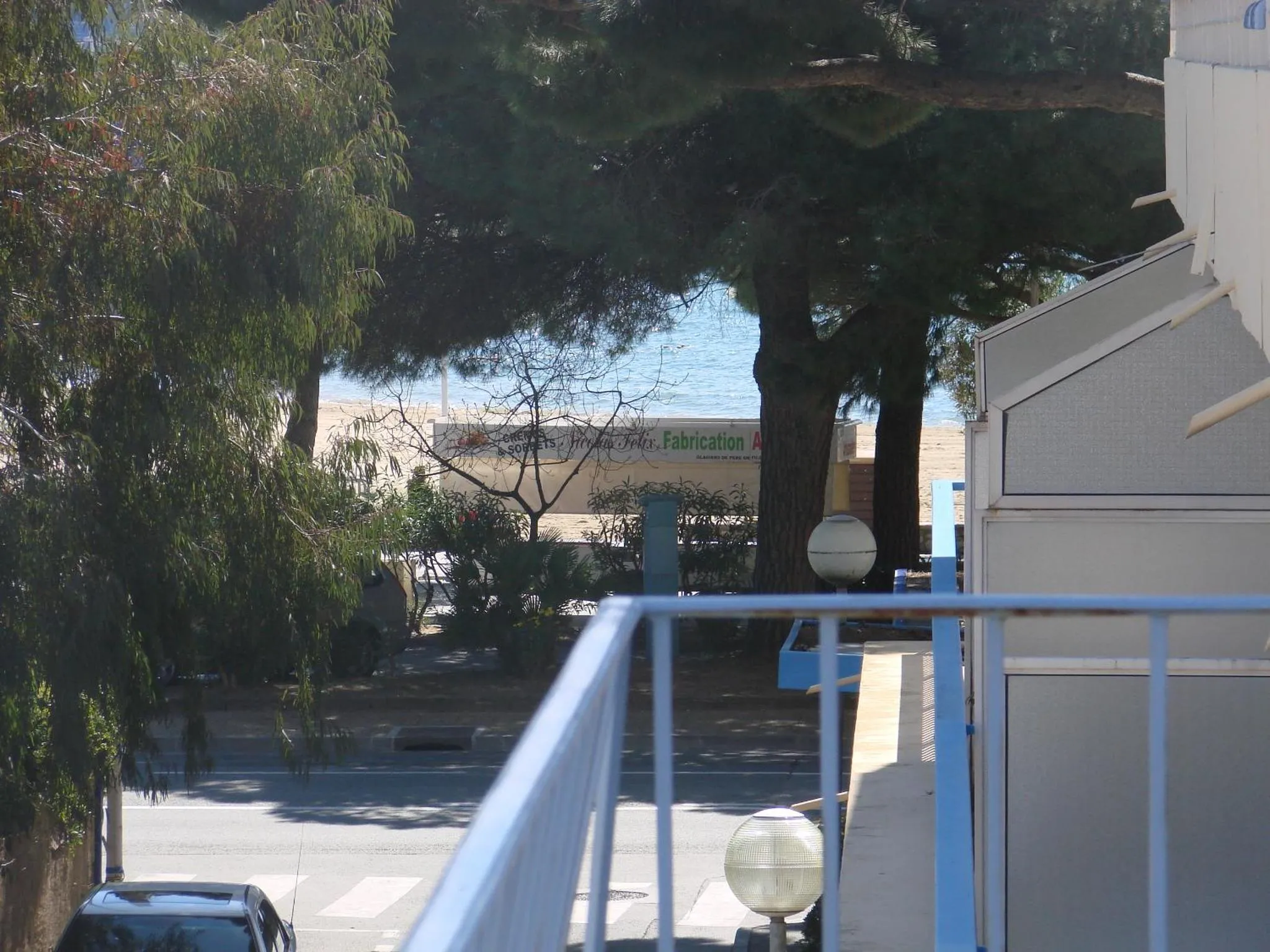 Vue d'une terrasse avec une rambarde blanche donnant sur une plage et la mer.