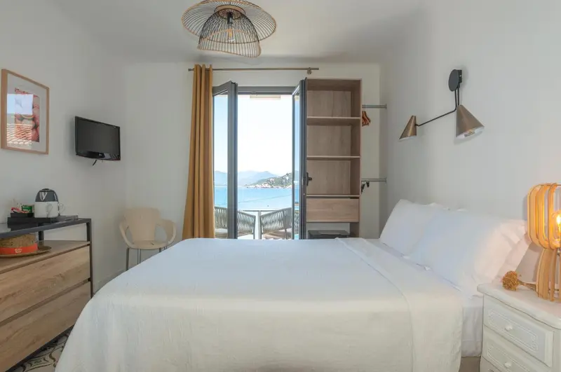 Une chambre lumineuse avec un lit blanc donnant sur une vue mer.