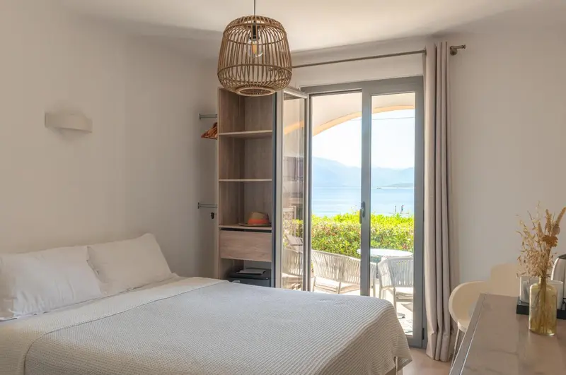 Une chambre lumineuse avec un lit fait et une vue sur la mer par une baie vitrée.