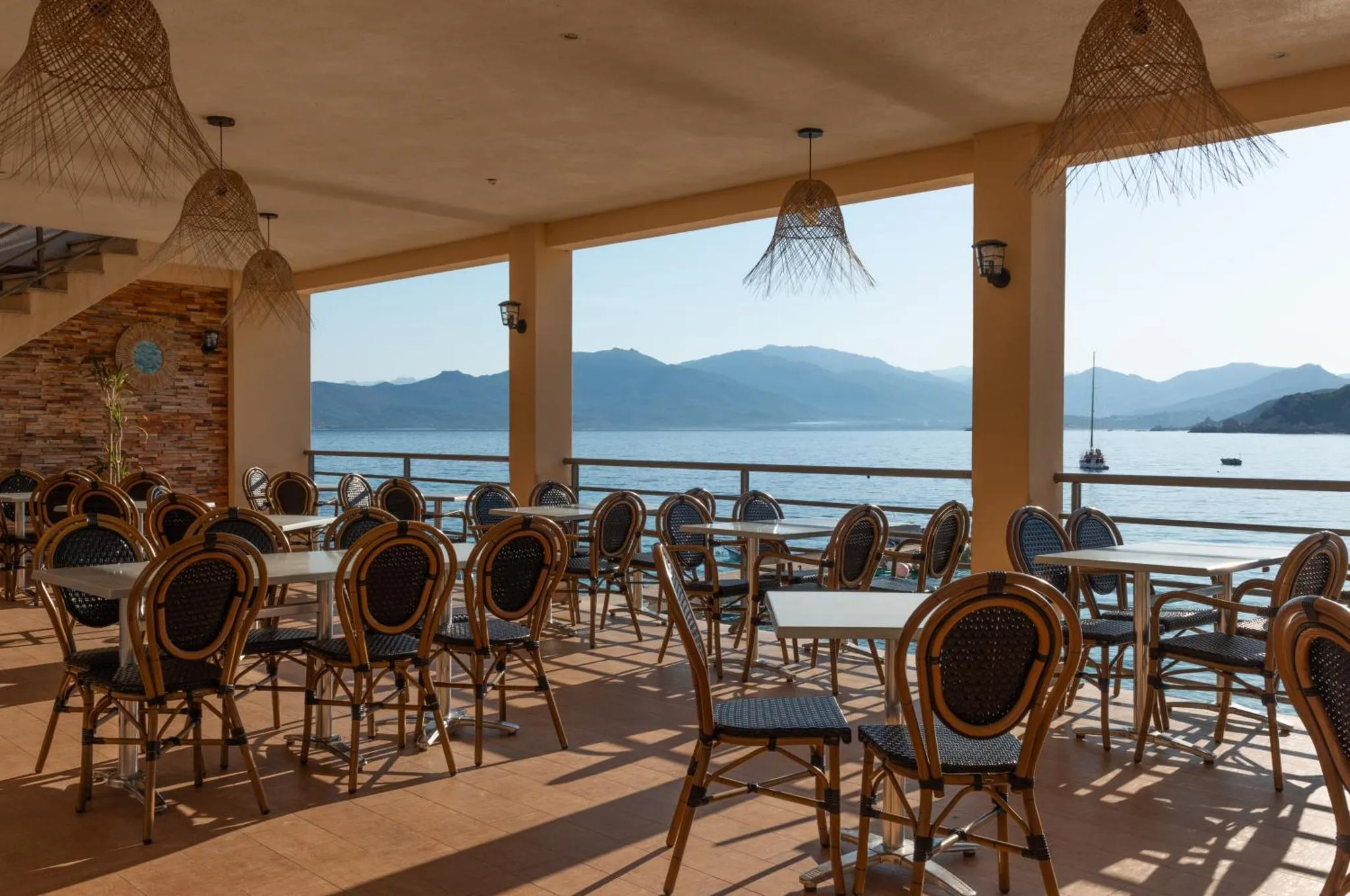 Terrasse ombragée avec tables et chaises donnant sur la mer.