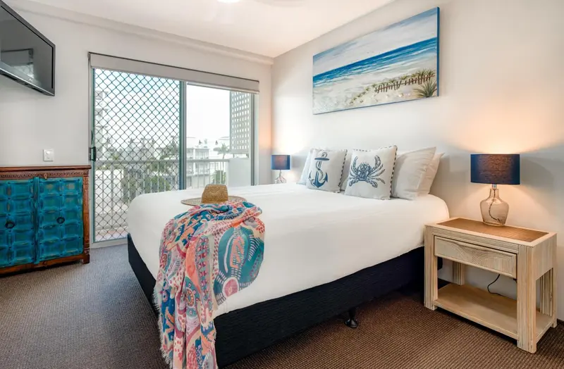 Une chambre lumineuse avec un grand lit recouvert d'une courtepointe et de coussins décoratifs.