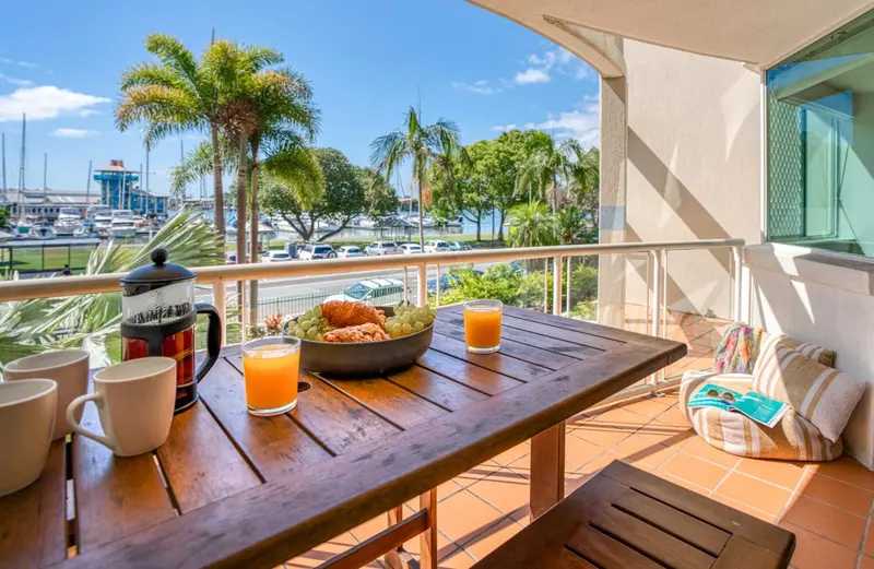 Une table en bois avec un petit-déjeuner est mise en scène sur une terrasse ensoleillée.