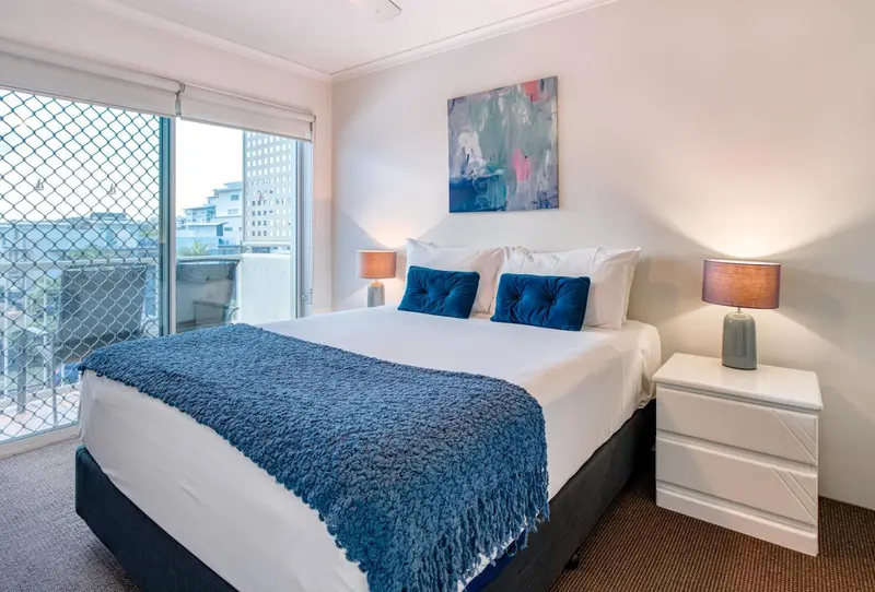 Une chambre lumineuse avec un grand lit et un accès à un balcon.