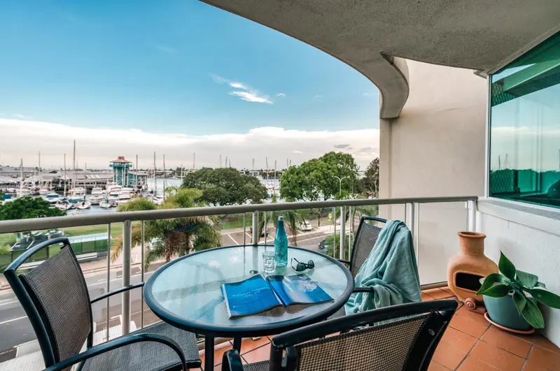 Une terrasse avec une table et des chaises offre une vue sur un port de plaisance et la mer.