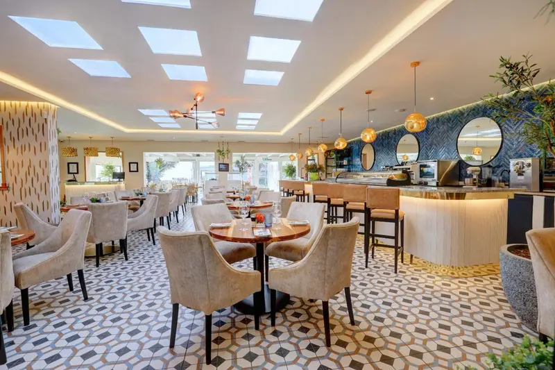 Une salle de restaurant lumineuse avec des tables dressées et un comptoir de bar.