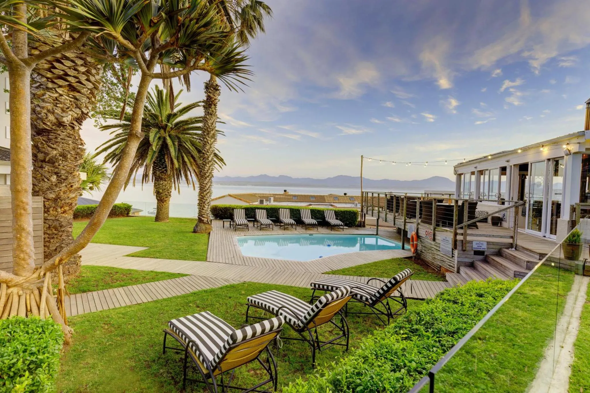 Jardin verdoyant avec piscine et transats face à la mer.