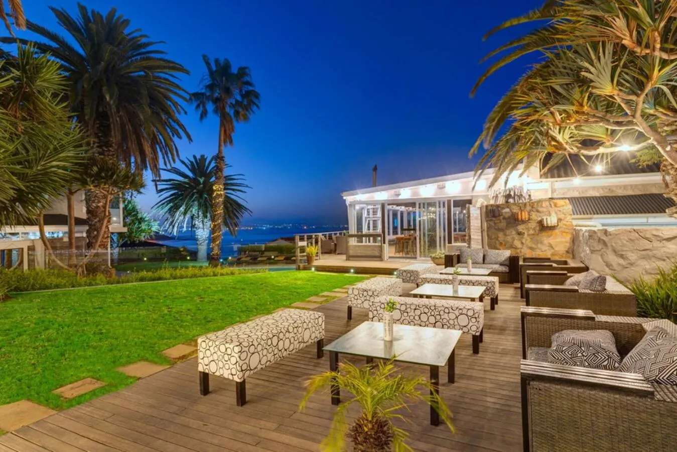 Terrasse aménagée avec mobilier de jardin et vue sur la mer au crépuscule.