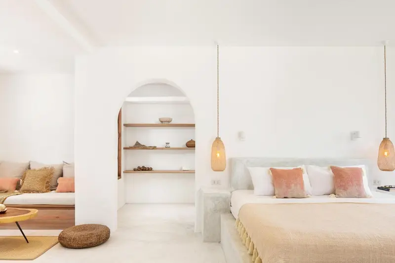 Chambre lumineuse aux murs blancs avec un lit et un espace détente.