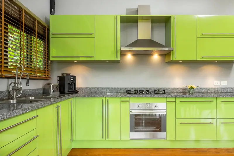 Cuisine moderne avec des armoires vert vif et un plan de travail en granit.