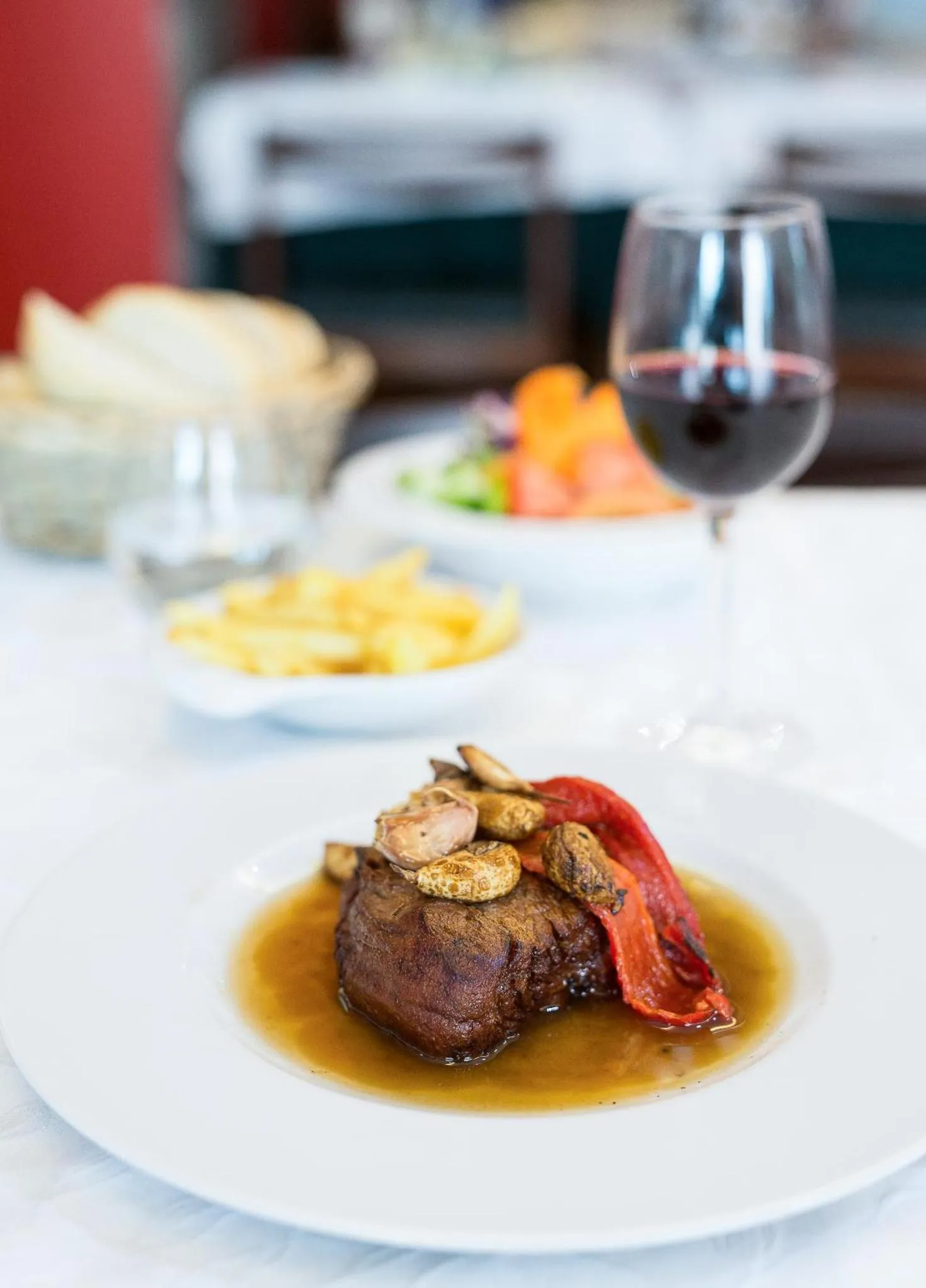 Assiette de viande accompagnée de légumes et de frites, avec un verre de vin rouge.