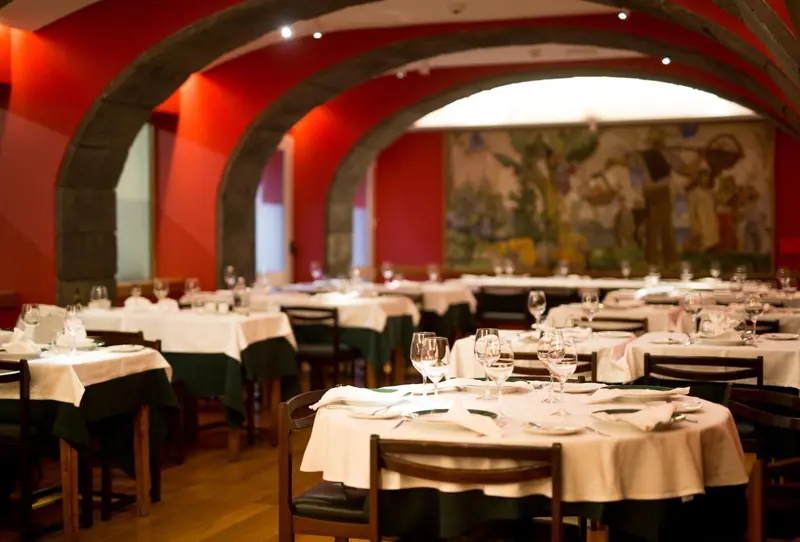 Une salle de restaurant avec des tables dressées et des arches en pierre.
