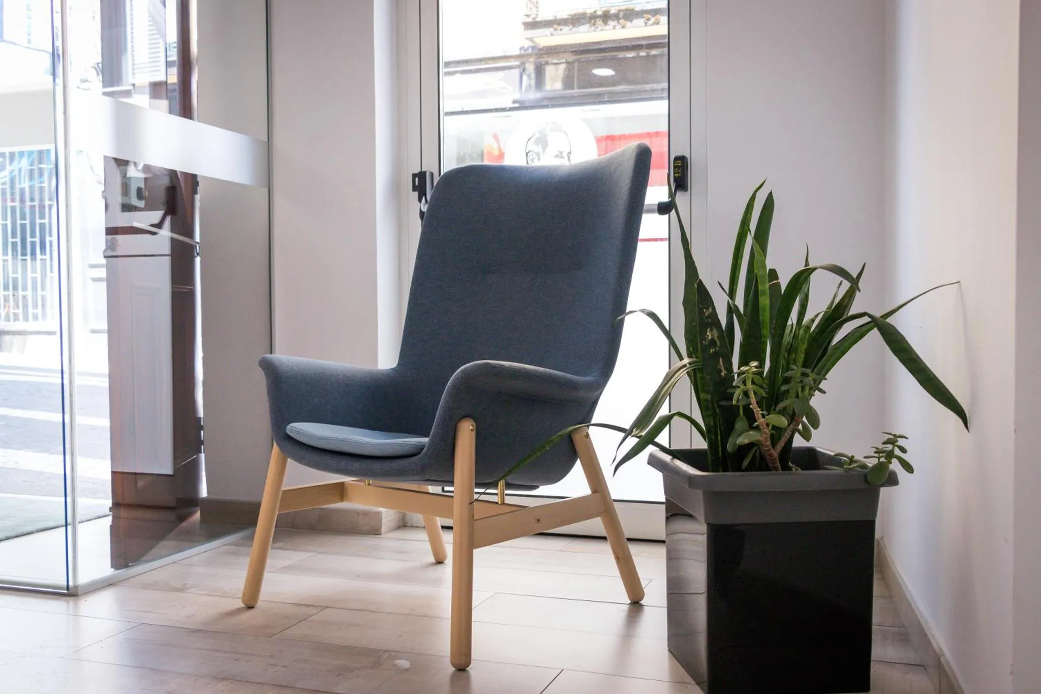 Un fauteuil bleu moderne est placé près d'une fenêtre et d'une plante verte en pot.