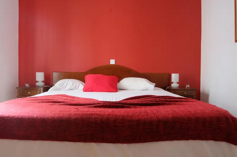 Une chambre avec un grand lit recouvert d'une couverture rouge et de coussins blancs.