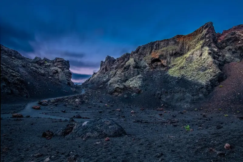Paysage volcanique sombre avec des formations rocheuses escarpées et un ciel nuageux.