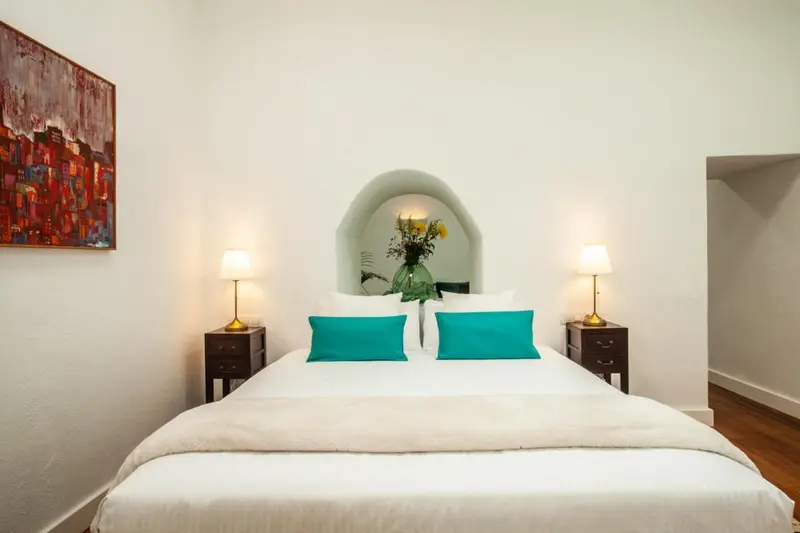 Une chambre lumineuse avec un grand lit recouvert d'une couverture blanche et de coussins turquoise.
