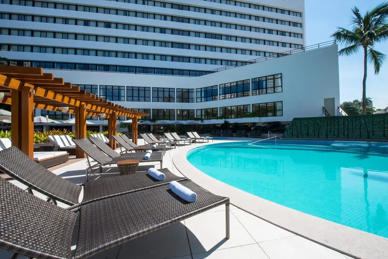 Transats et parasols disposés autour d'une piscine turquoise devant un bâtiment moderne.