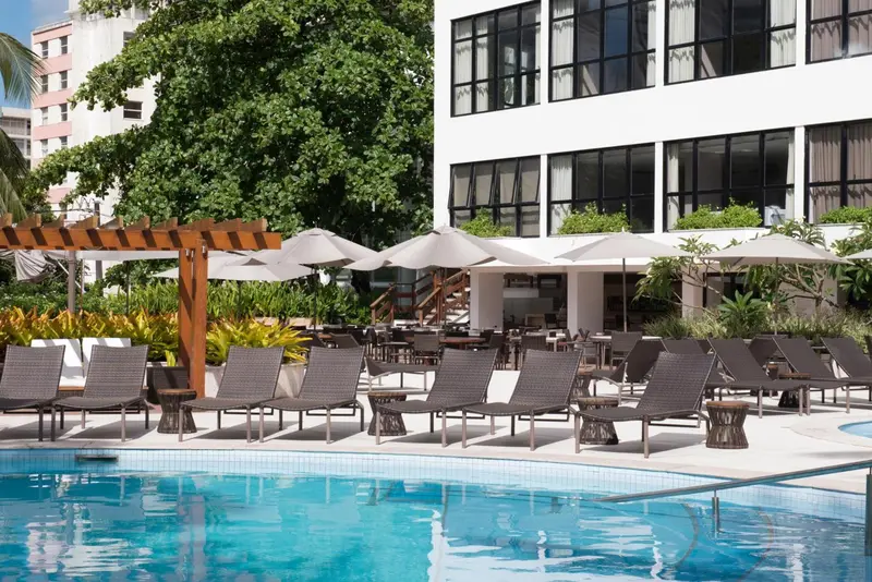 Transats et parasols disposés autour d'une piscine turquoise dans un jardin luxuriant.