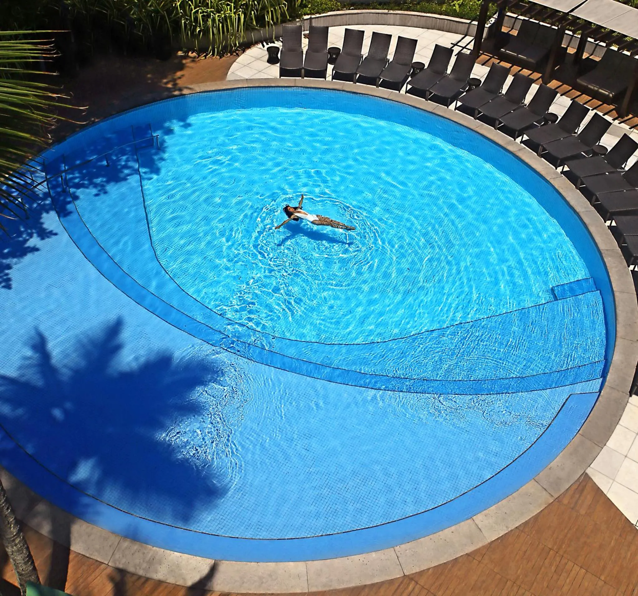 Une personne se détend dans une piscine circulaire entourée de chaises longues.