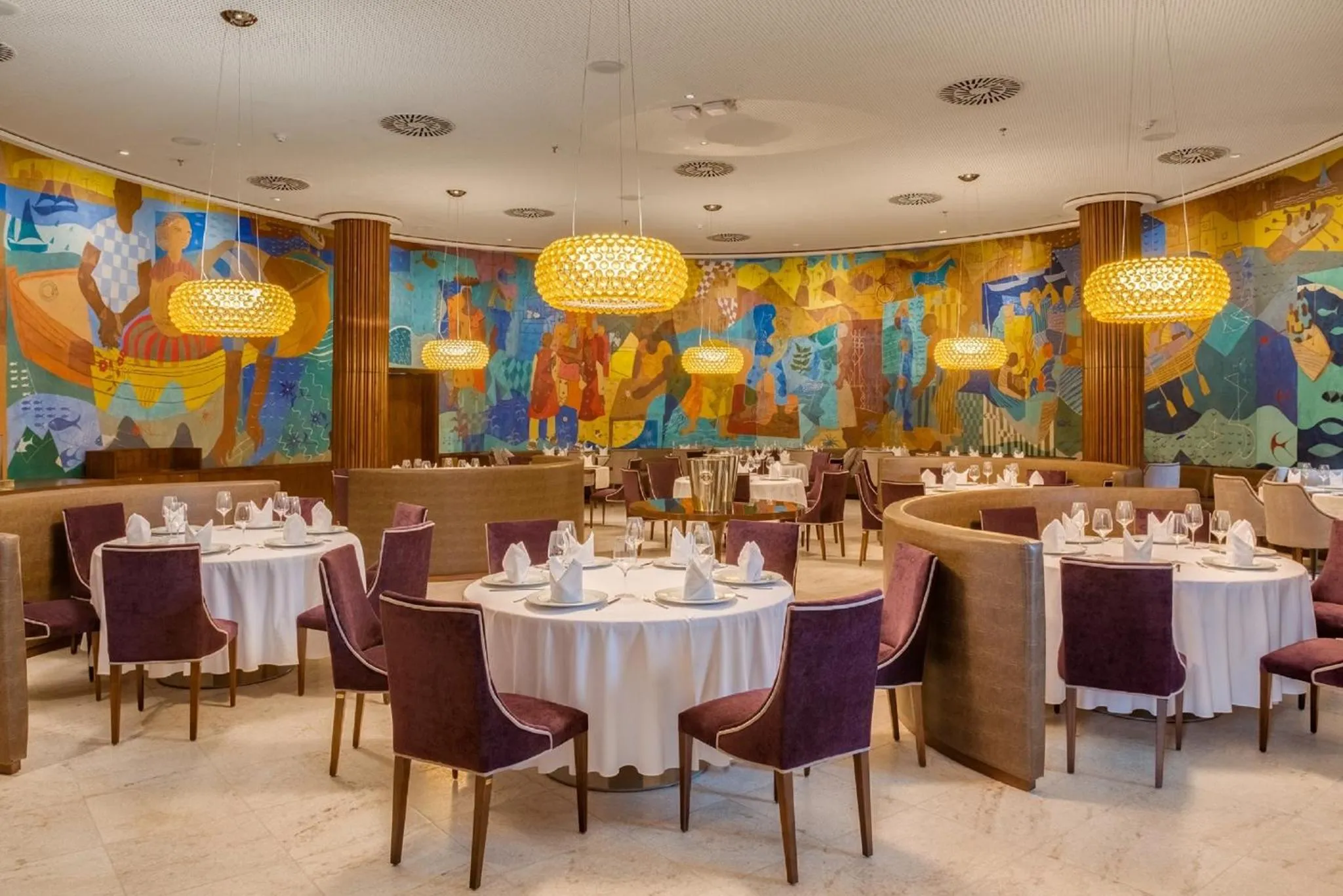 Une salle de restaurant lumineuse avec des tables dressées et une décoration murale colorée.
