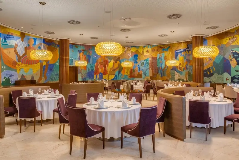 Une salle de restaurant lumineuse avec des tables dressées et une décoration murale colorée.