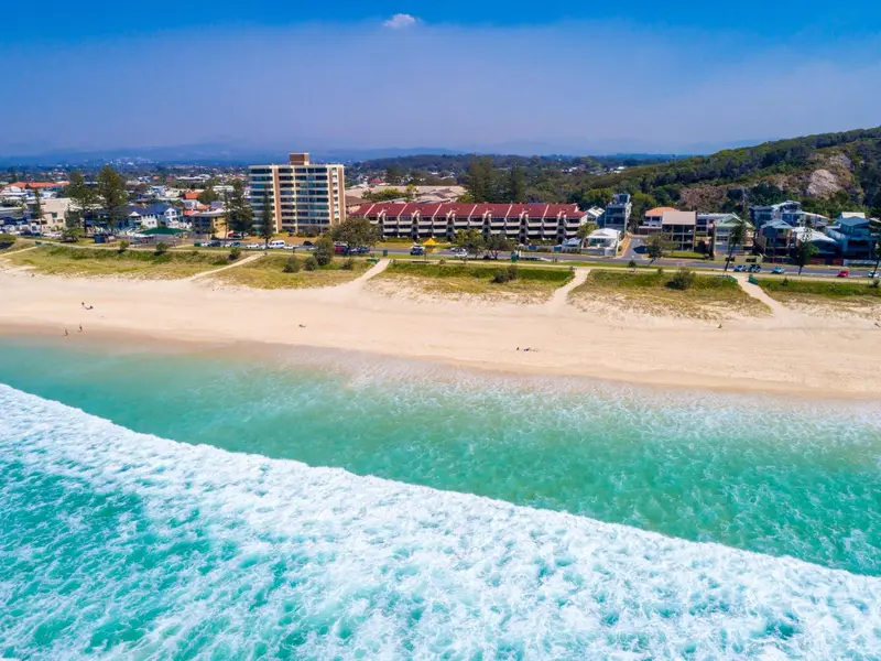 Vue aérienne d'une plage de sable fin bordée d'une eau turquoise et d'une station balnéaire.