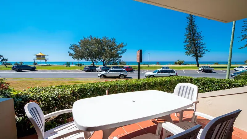 Terrasse avec table et chaises donnant sur une plage et une route côtière.