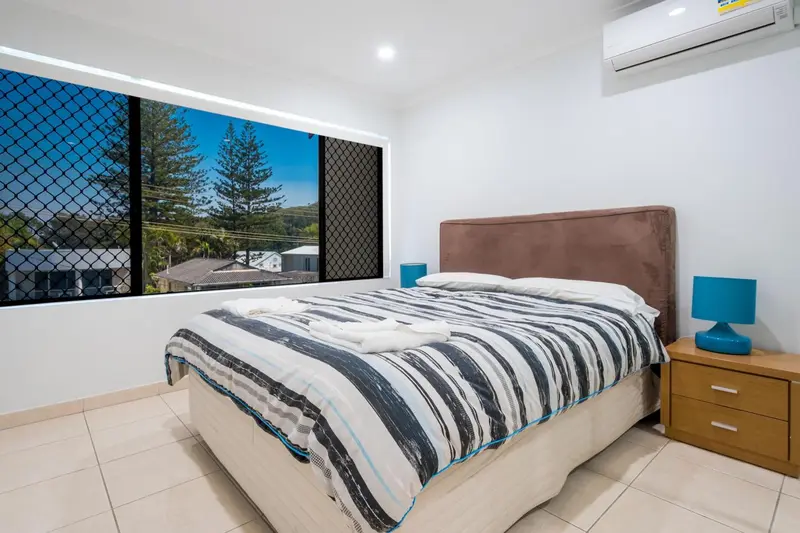 Une chambre lumineuse avec un lit recouvert d'une courtepointe rayée et une vue sur la végétation.