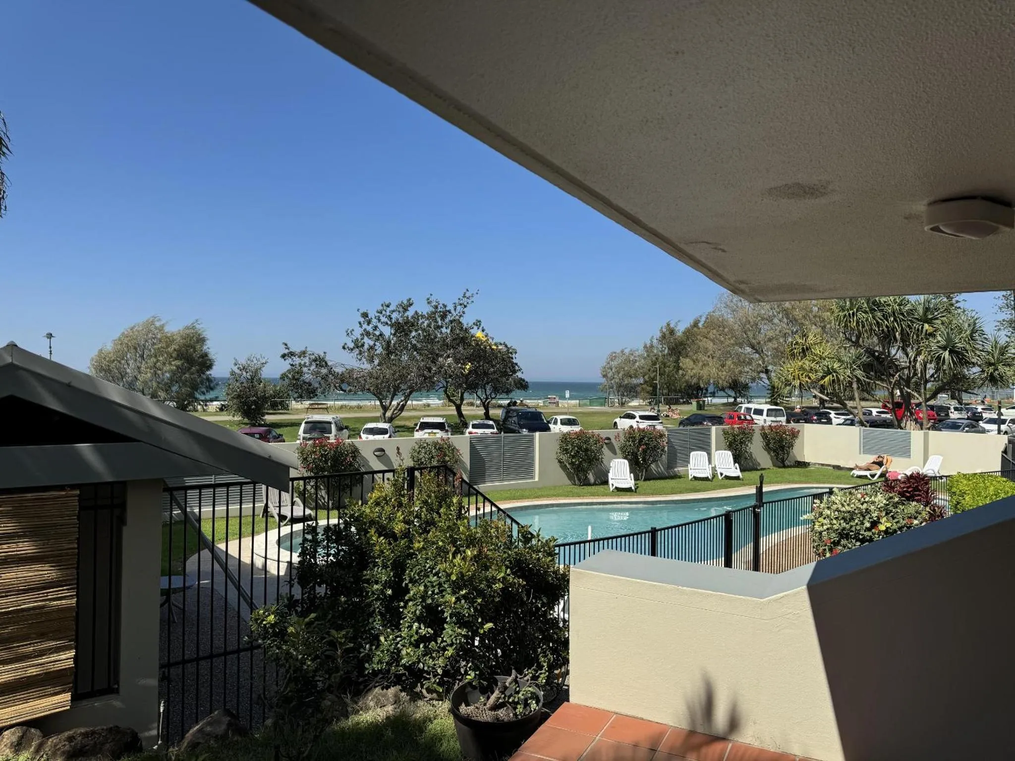 Vue sur une piscine et la mer depuis une terrasse ombragée.