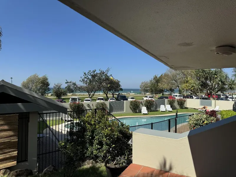 Vue sur une piscine et la mer depuis une terrasse ombragée.