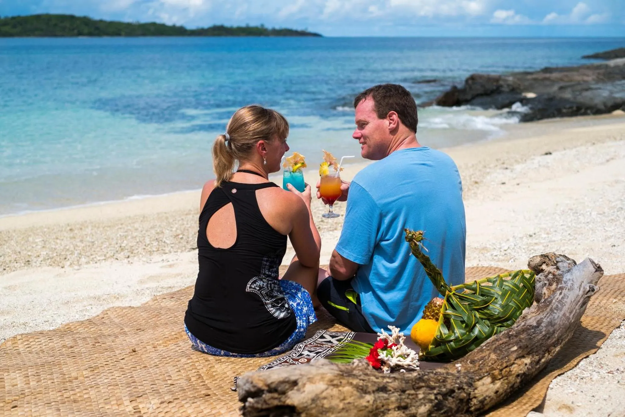 Un couple déguste des cocktails sur une plage de sable blanc.