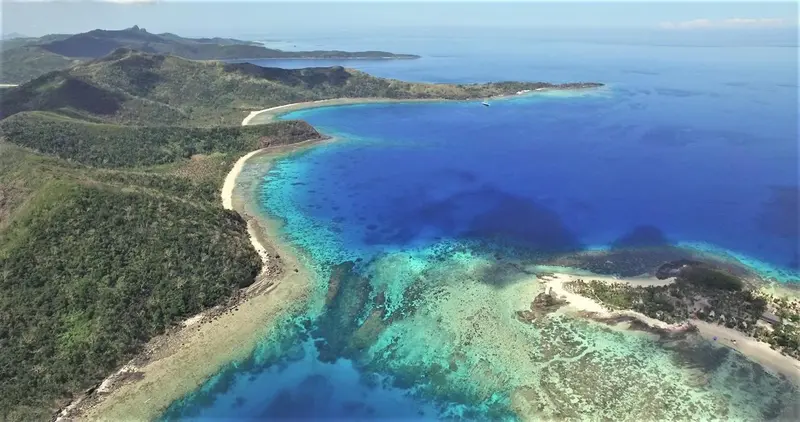 Vue aérienne d'une côte tropicale avec une plage de sable et des eaux turquoise.