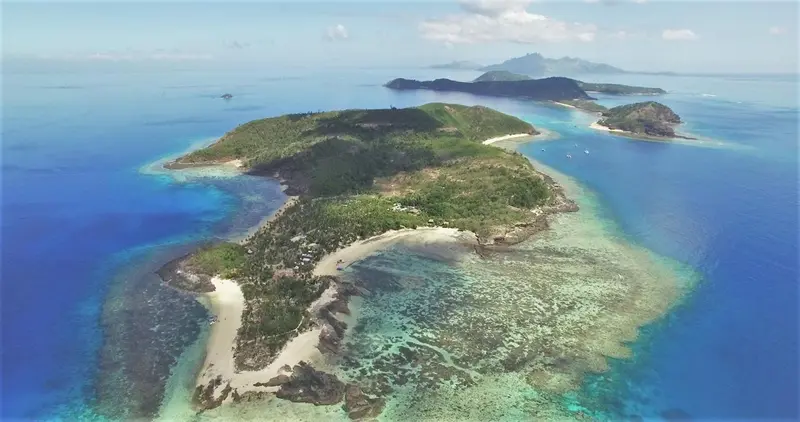 Vue aérienne d'une île tropicale entourée d'eaux turquoise et de récifs coralliens.