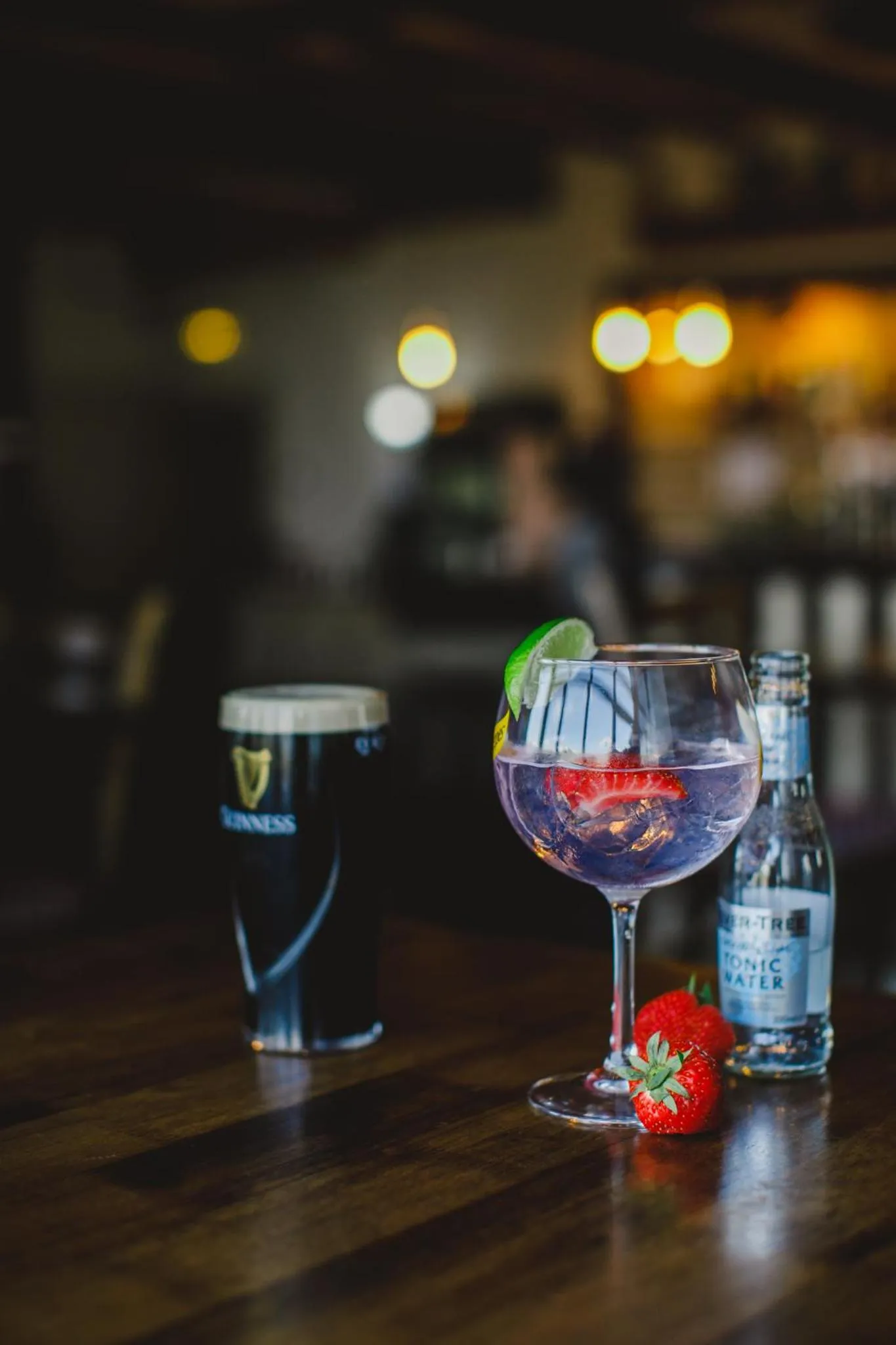 Un cocktail et une bière sont posés sur un comptoir en bois sombre.