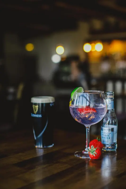 Un cocktail et une bière sont posés sur un comptoir en bois sombre.