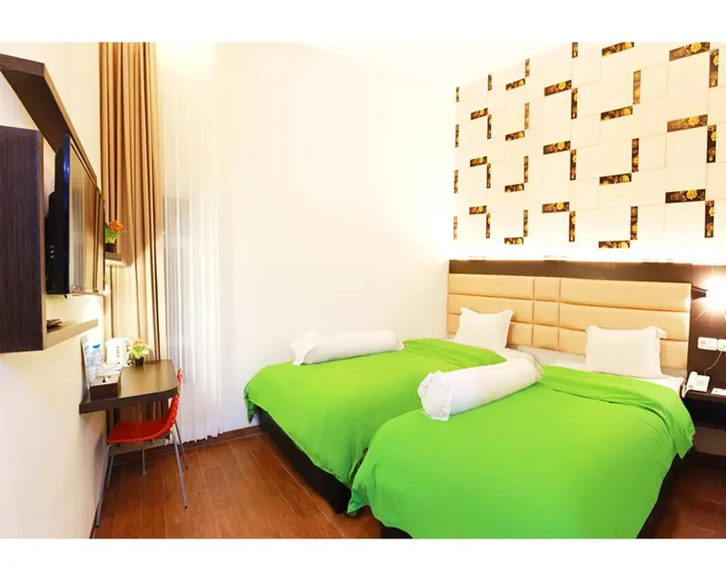Chambre lumineuse avec deux lits verts et un mur décoratif.