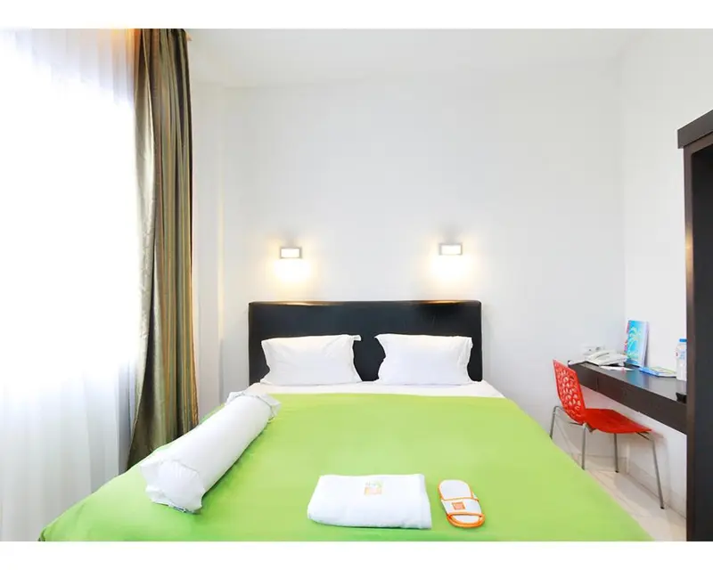Une chambre lumineuse avec un lit recouvert d'un drap vert vif et un bureau.