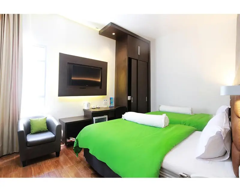Une chambre lumineuse avec un lit recouvert d'une couverture verte et un fauteuil.