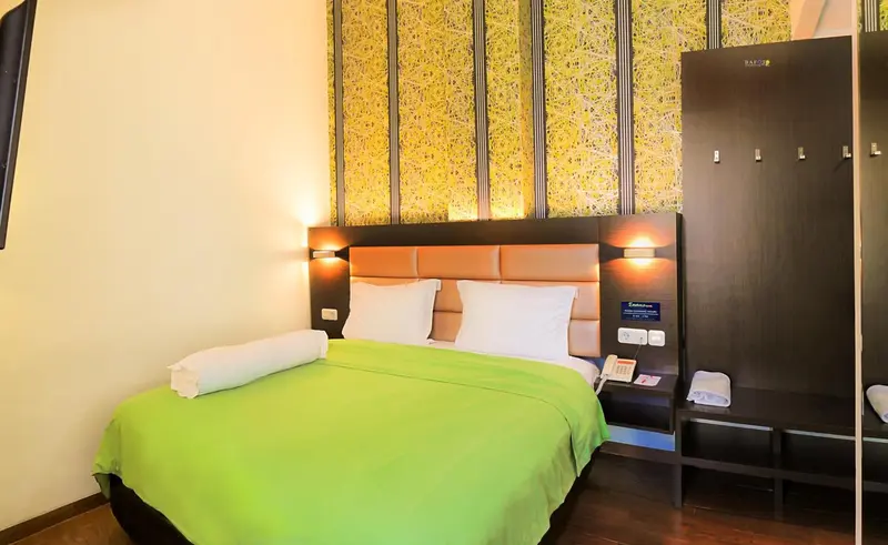 Une chambre lumineuse avec un lit recouvert d'une couverture verte et un mur décoratif jaune.