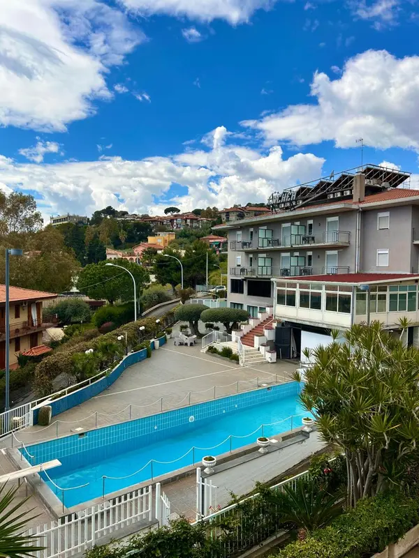 Vue aérienne d'une piscine d'hôtel entourée de végétation et surplombant un paysage urbain.
