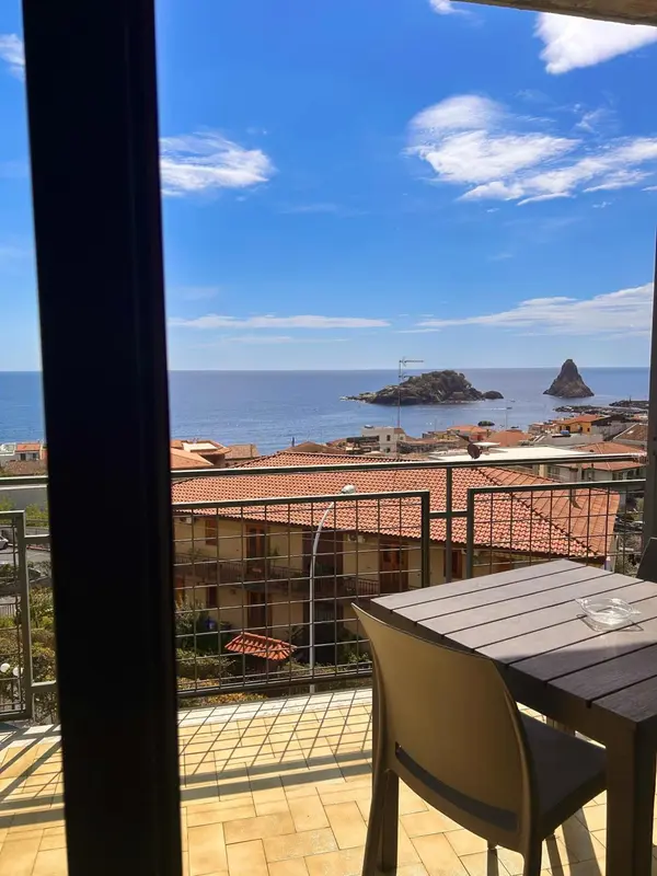 Vue sur la mer et un îlot rocheux depuis une terrasse avec table et chaises.