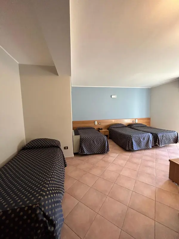 Chambre avec trois lits simples et un carrelage ocre.
