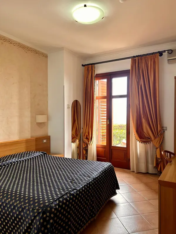 Une chambre avec un lit recouvert d'une couverture sombre et une porte-fenêtre donnant sur l'extérieur.