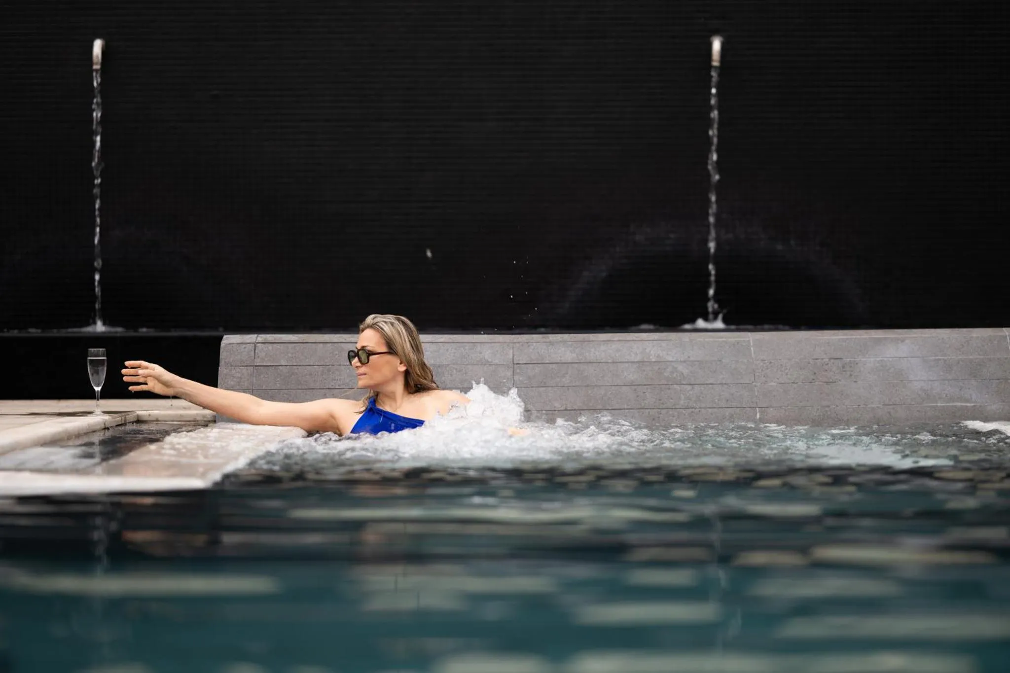 Une personne se détend dans une piscine avec des jets d'eau et un verre à la main.