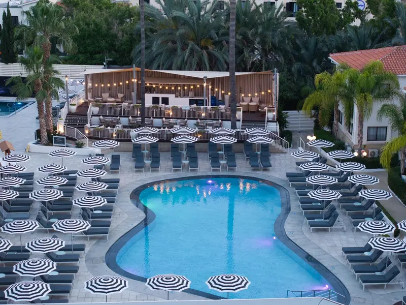 Une piscine rectangulaire bordée de transats et de parasols rayés blancs et noirs.
